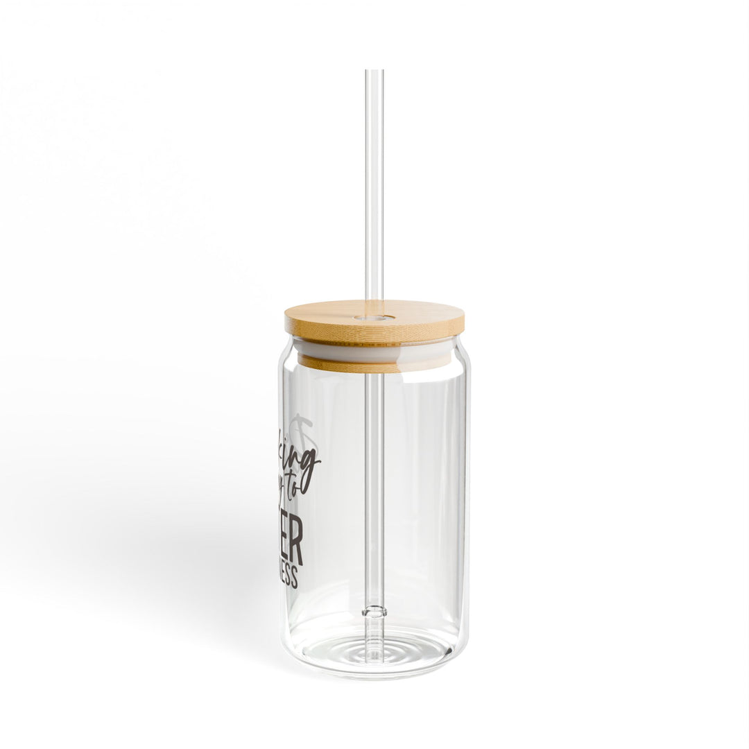 A clear tempered glass sipper with a bamboo lid and a plastic straw, featuring text that reads &