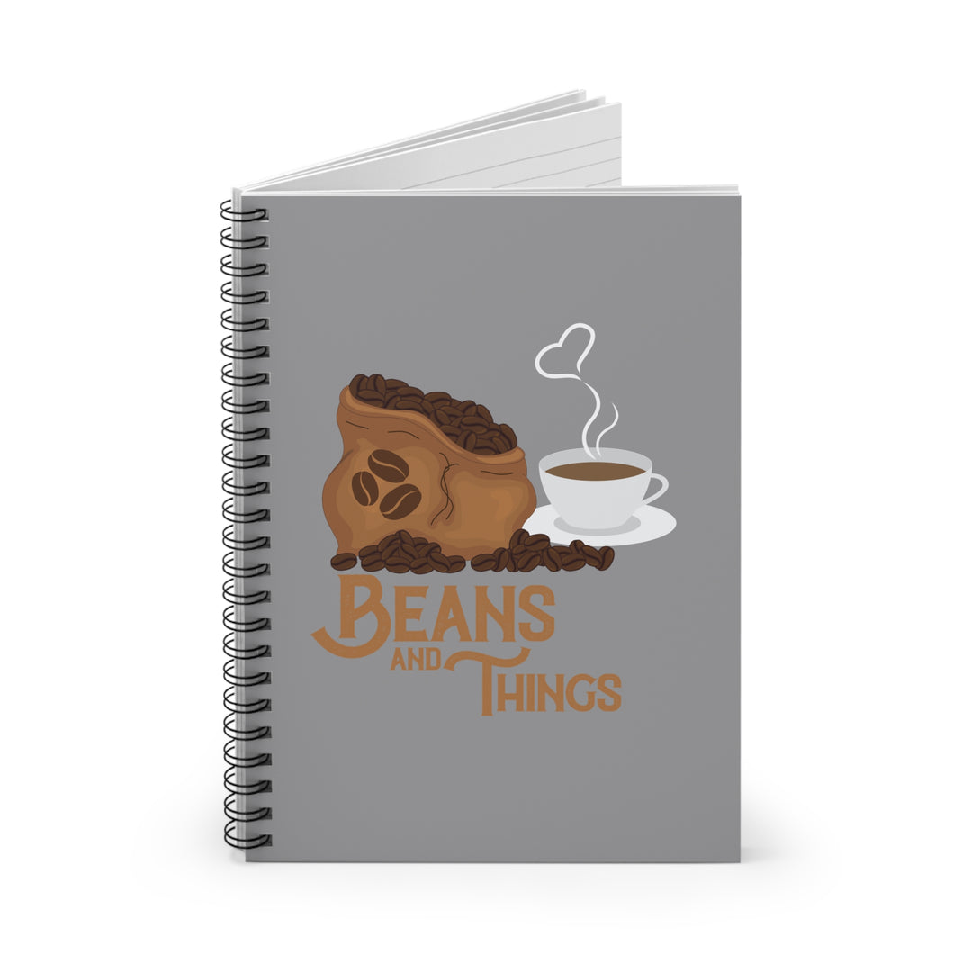 A spiral notebook with a dark grey back cover and a front cover print featuring a stylized design with the text 'BEANS AND THINGS' and an illustration of a cup of coffee and beans.