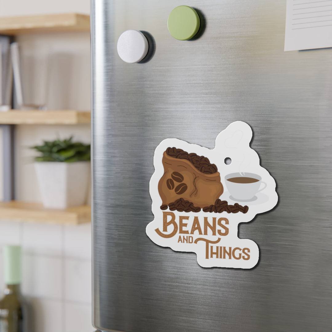 A magnet with an illustration of a coffee cup and beans, with the text 'BEANS AND THINGS' on a refrigerator.