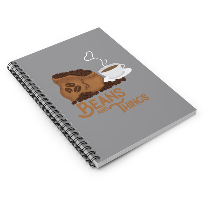 A spiral notebook with a dark grey back cover and a front cover print featuring a stylized design with the text &