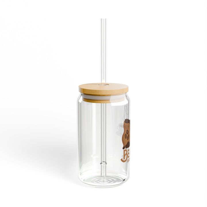 A clear tempered glass sipper with a bamboo lid and a plastic straw, featuring printed text &
